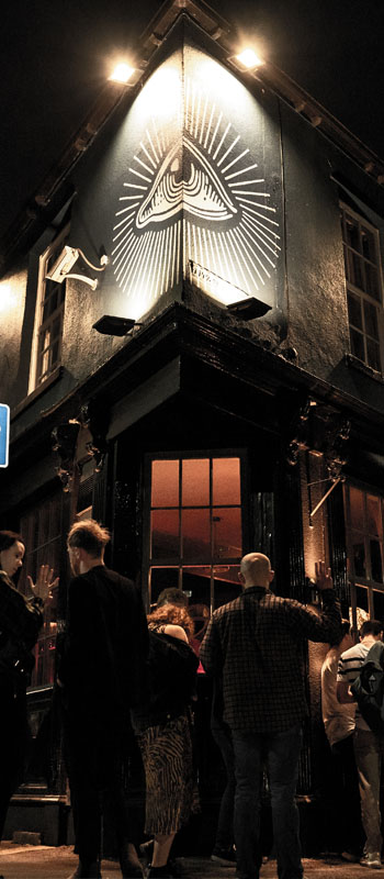 photograph of a group of people stood outside a the corner of a pub in the evening