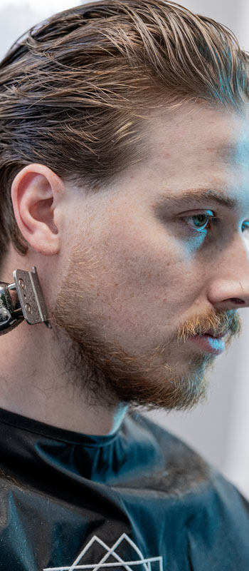 photograph of a man having his beard groomed by a barber